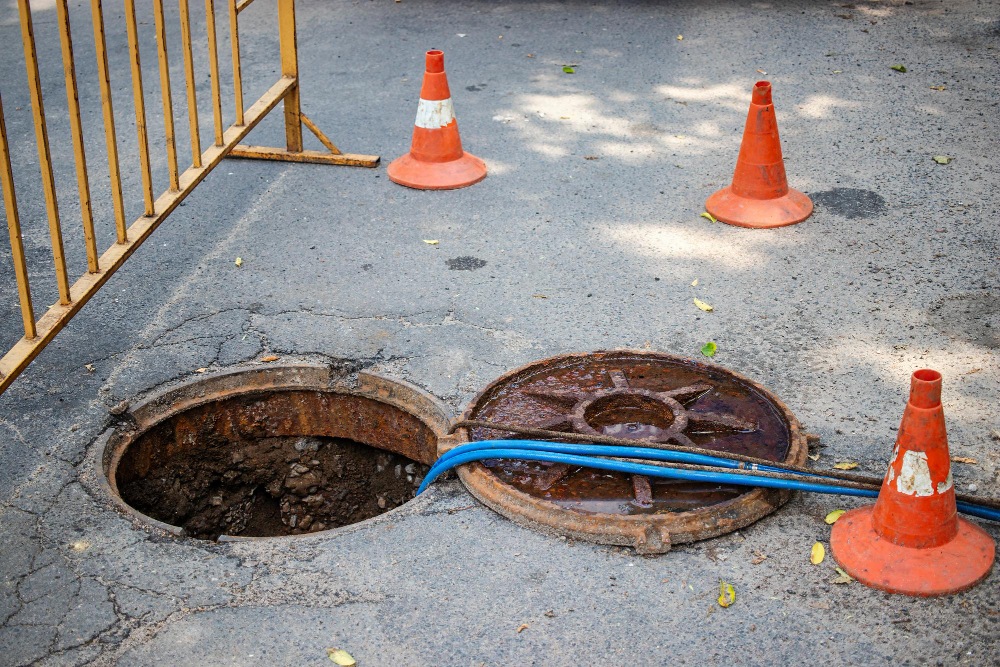 Bueiro aberto com cones de sinalização em via urbana.